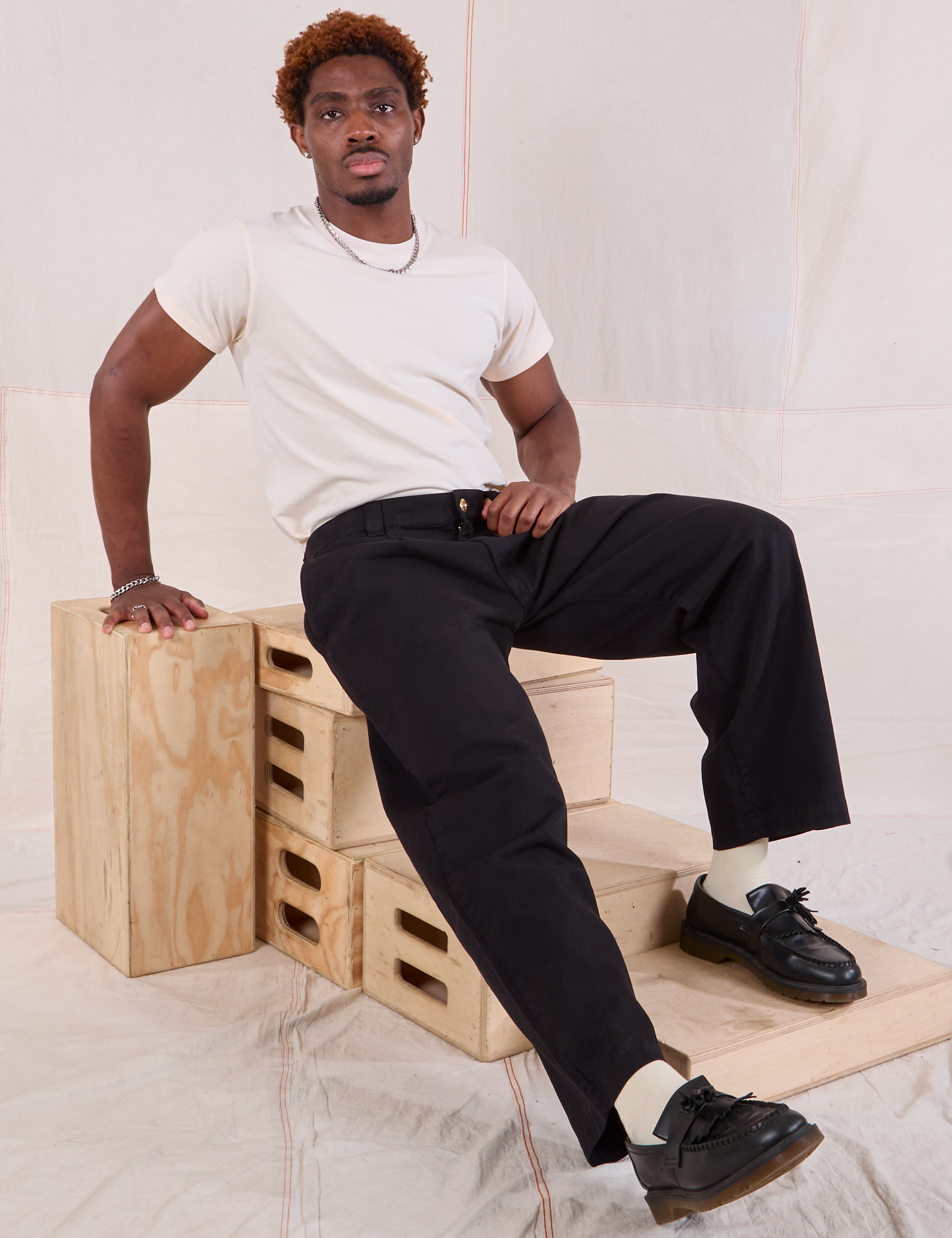 Issac is wearing Mid-Rise Pleated Trousers in Basic Black and Organic Vintage Tee in vintage tee off-white