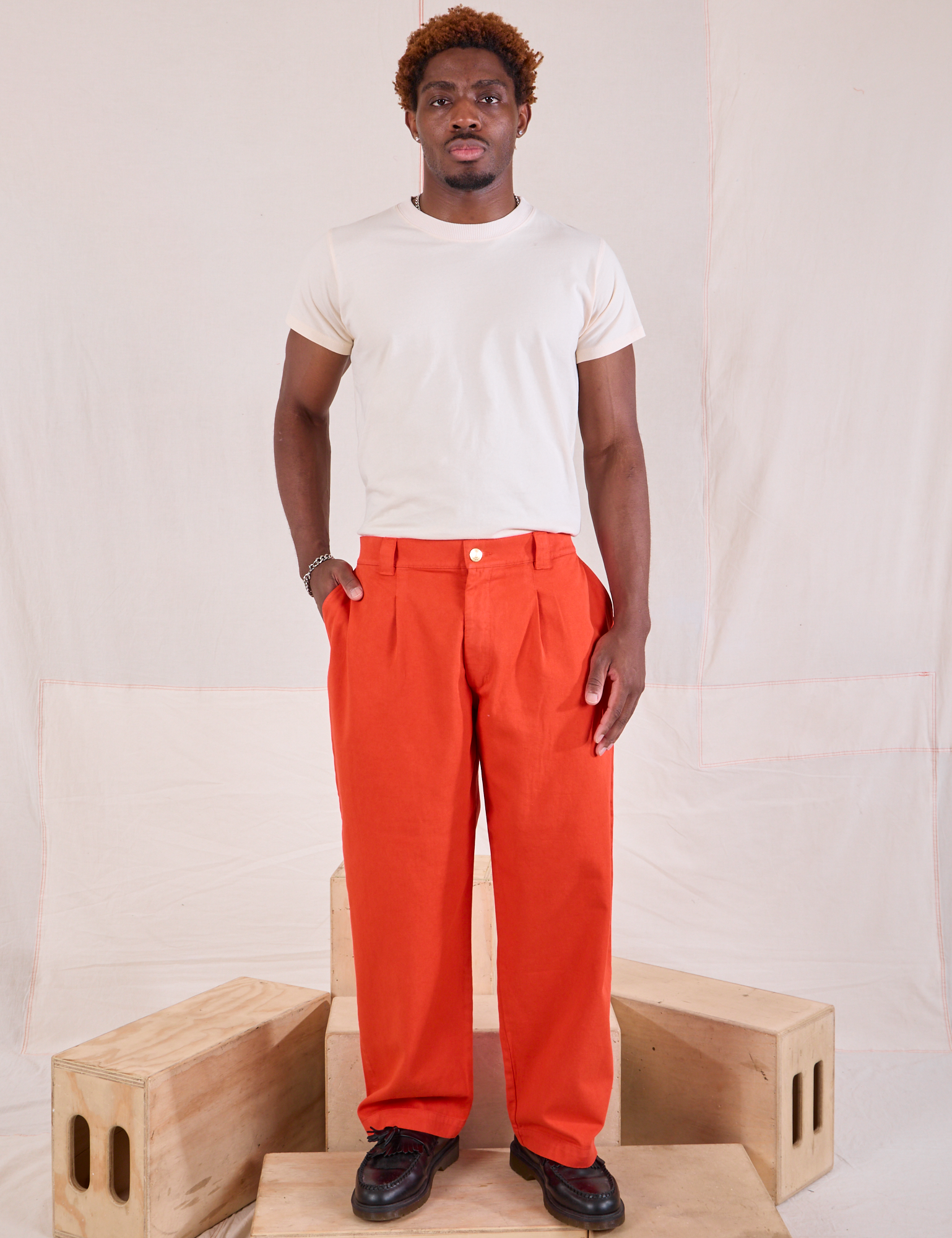 Issac is wearing Mid-Rise Pleated Trousers in Chili Red and Organic Vintage Tee in vintage tee off-white