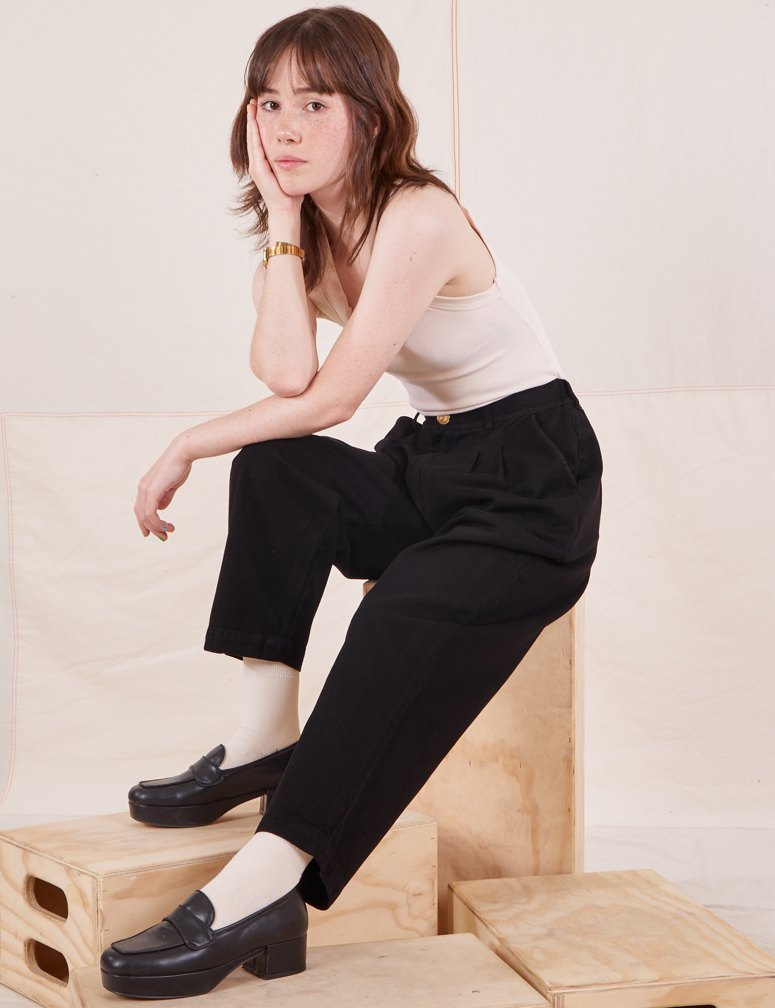 Hana is sitting on a wooden crate wearing Organic Trousers in Basic Black