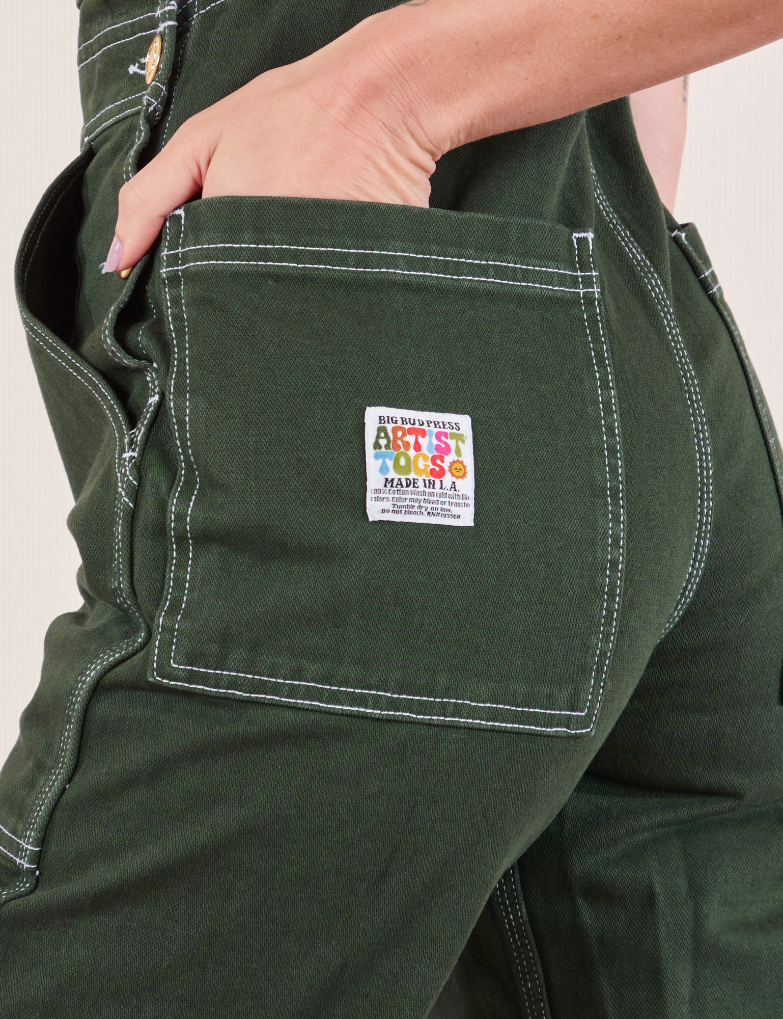 Original Overalls in Swamp Green back pocket close up. Alex has her hand in the pocket.