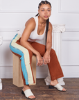 Gabi is sitting on a wooden crate wearing Hand-Painted Stripe Western Pants in Burnt Terracotta and vintage off-white Tank Top