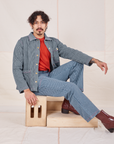 Jesse is sitting sideways on a wooden crate wearing Railroad Stripe Denim Work Jacket paired with matching Work Pants