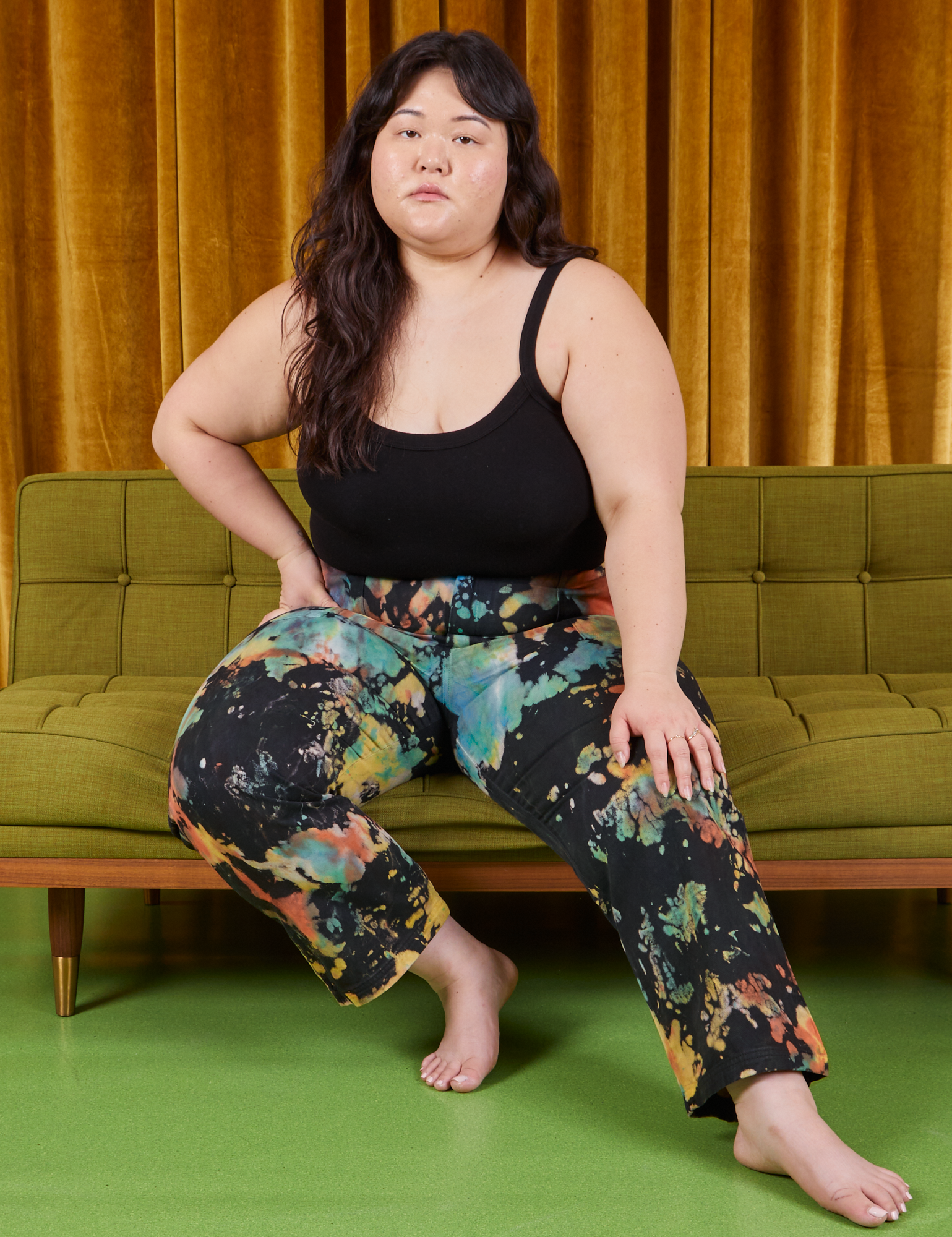 Ashley is sitting on a green couch. She is wearing Rainbow Magic Waters Work Pants and black Cropped Cami