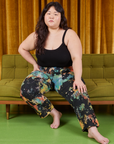 Ashley is sitting on a green couch. She is wearing Rainbow Magic Waters Work Pants and black Cropped Cami