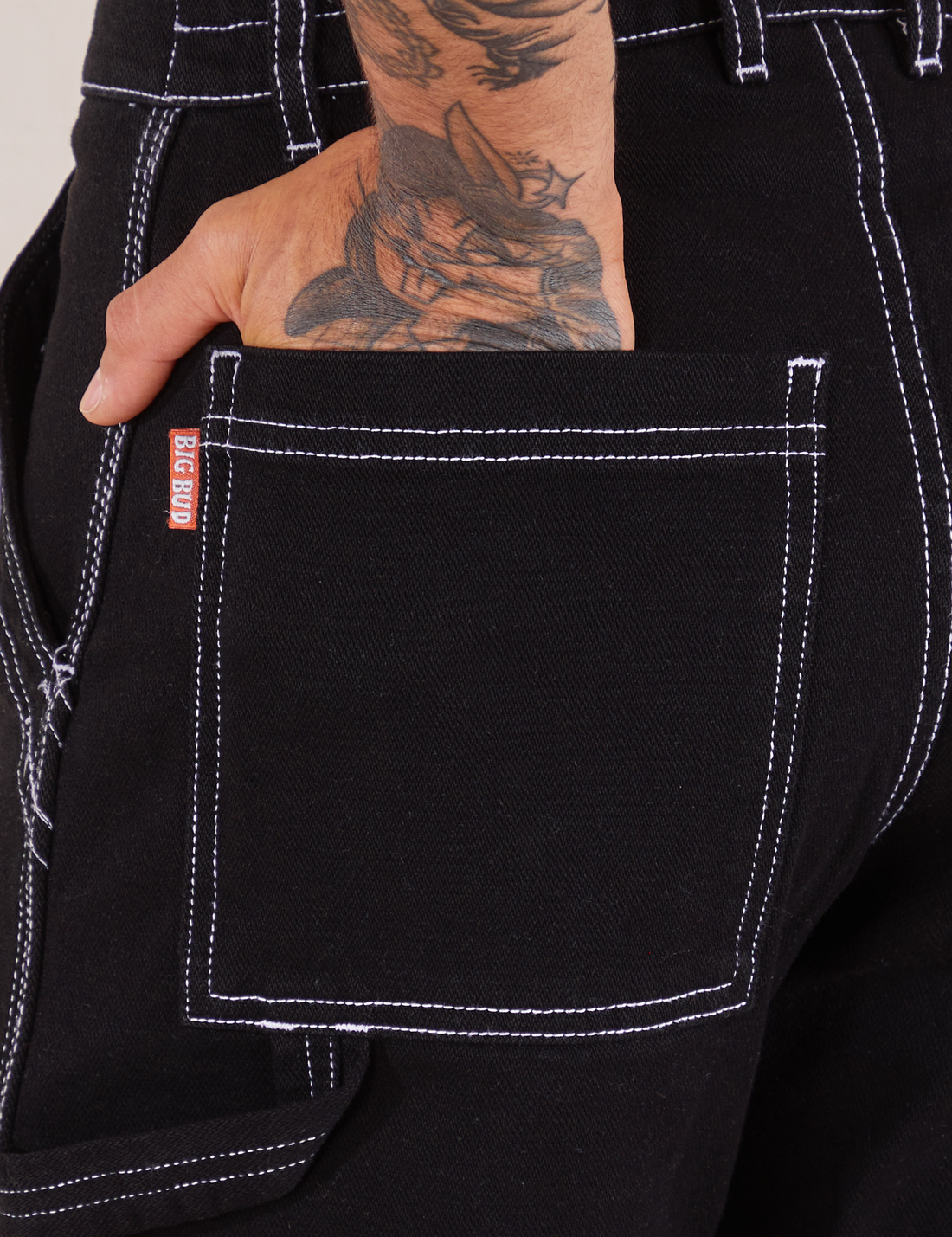 Carpenter Jeans in Black back pocket close up. Jesse has their hand in the pocket.