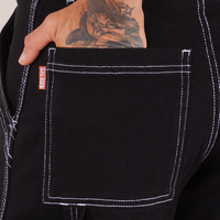 Carpenter Jeans in Black back pocket close up. Jesse has their hand in the pocket.