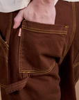 Close up of Quinn's hand in the back pocket of Carpenter Jeans in Fudgesicle Brown