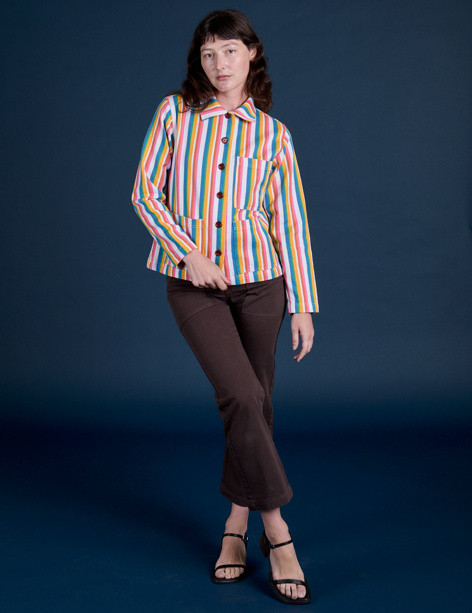 Alex is wearing a buttoned up Stripe Work Jacket in Rainbow Stripe paired with espresso brown Work Pants