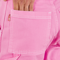 Carpenter Jeans in Bubblegum Pink back pocket close up. Jesse has their hand in the pocket.
