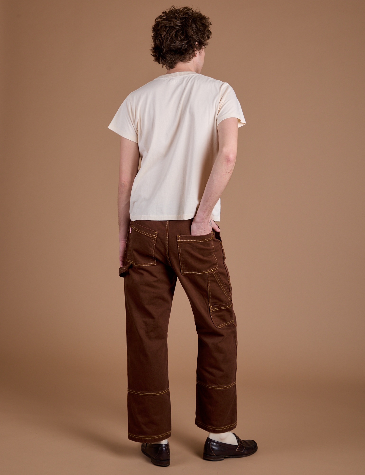 Back view of Carpenter Jeans in Fudgesicle Brown and Organic Vintage tee in Vintage Tee Off-White on Quinn