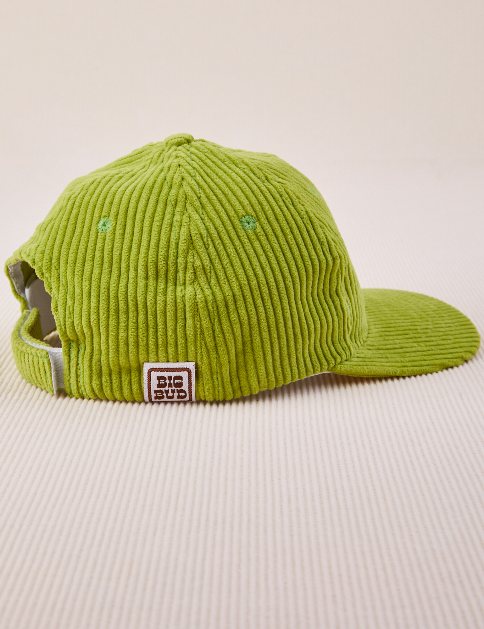 Side view of Dugout Corduroy Hat in Gross Green. Big Bud label sewn on edge of hat.