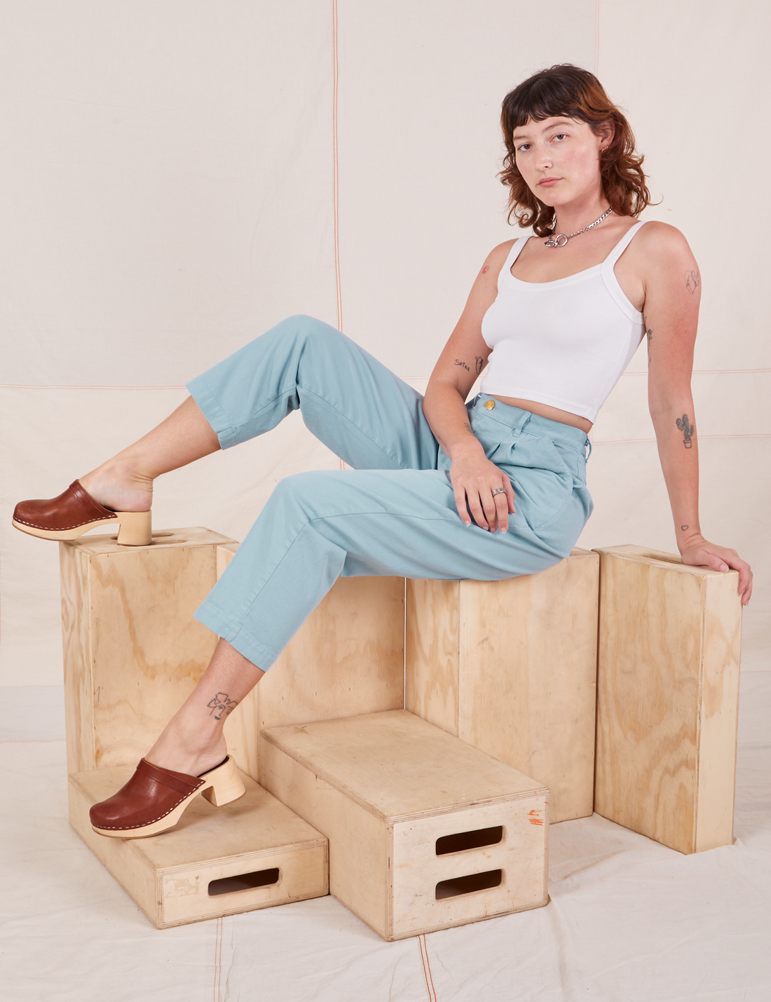 Alex is sitting on a wooden crate wearing Heavyweight Trousers in Baby Blue and vintage off-white Cropped Cami