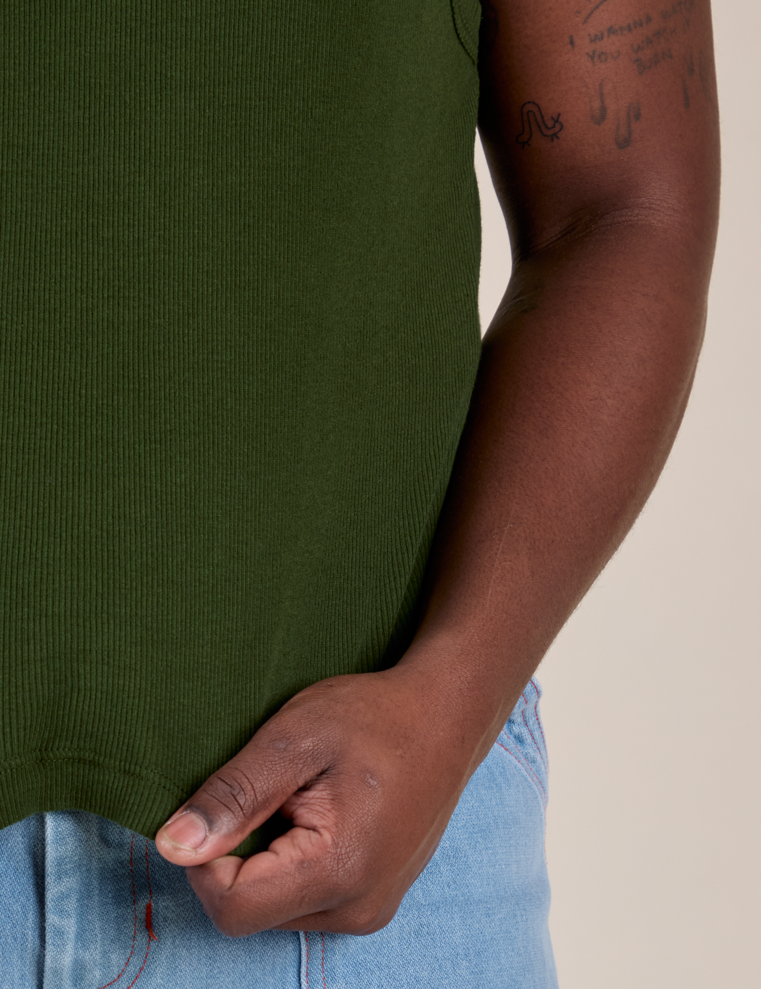 Close up of Demi holding the bottom hem of Muscle Tee in Evergreen