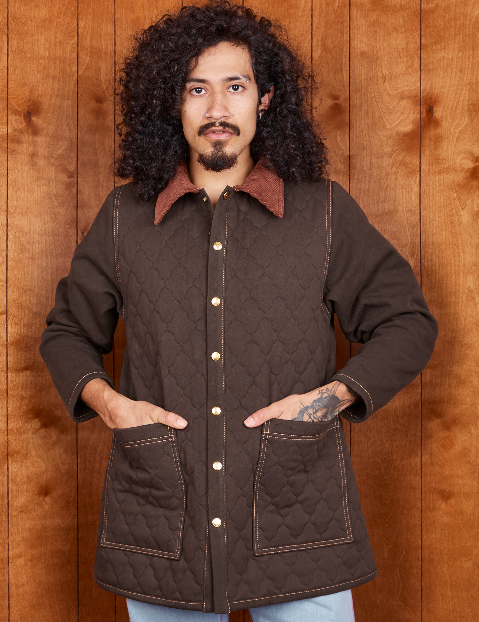 Jesse is wearing a buttoned up Quilted Overcoat in Espresso Brown. Both their hands are in the pockets.