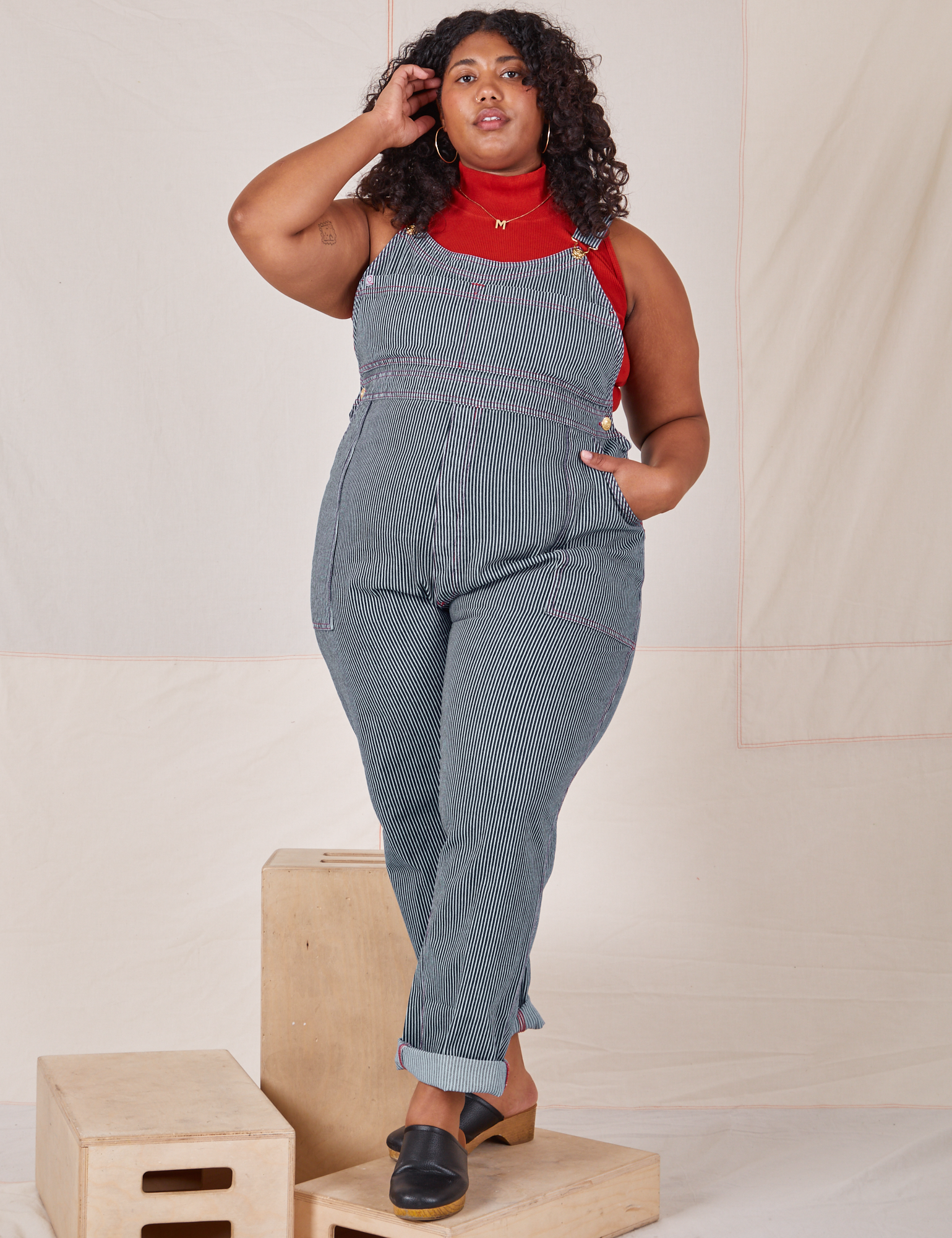 Morgan is 5&#39;5&quot; and wearing 1XL Railroad Stripe Denim Original Overalls paired with a paprika Sleeveless Turtleneck