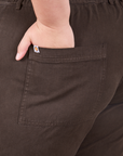 Back pocket close up of Short Sleeve Jumpsuit in Espresso Brown. Marielena has her hand in the pocket.