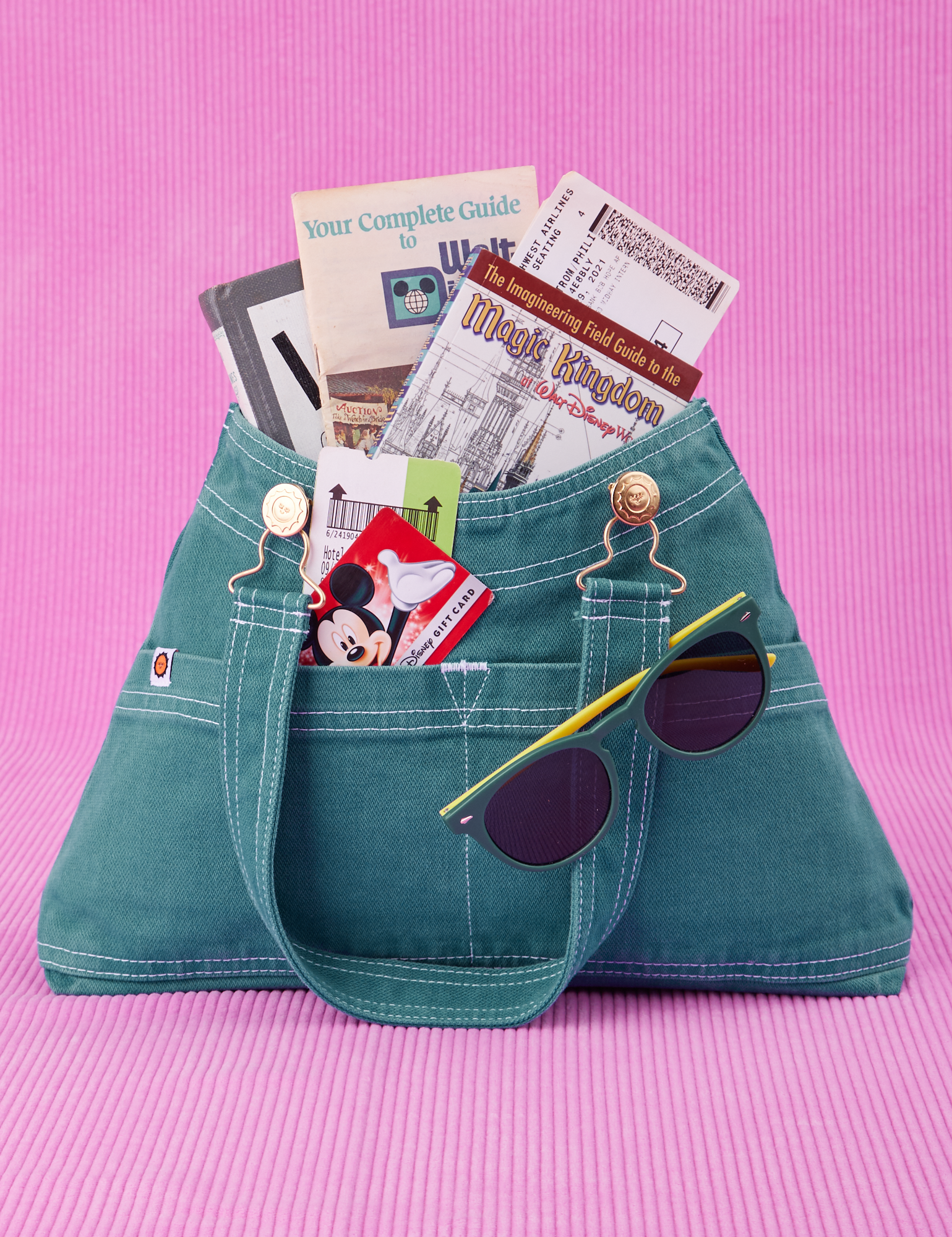 Overall Handbag in Marine Blue. Magic Kingdom brochures inside main compartment. Disney gift card in front pocket and sunglasses