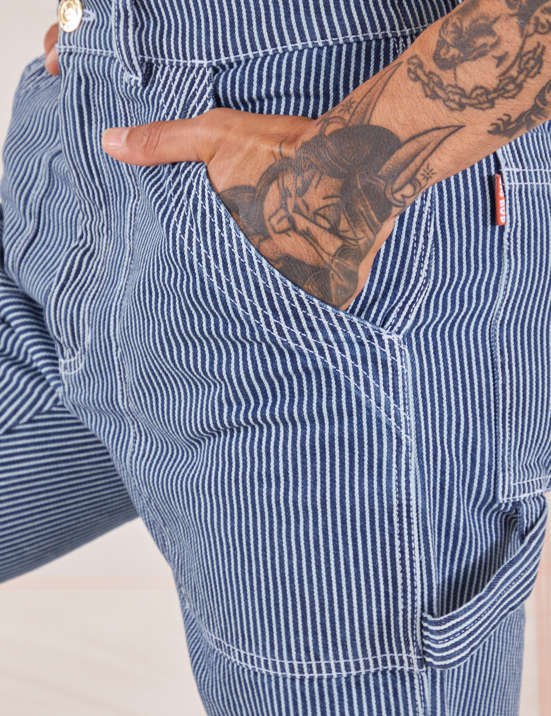 Carpenter Jeans in Railroad Stripes front pocket close up. Jesse has their hand tucked into the pocket.