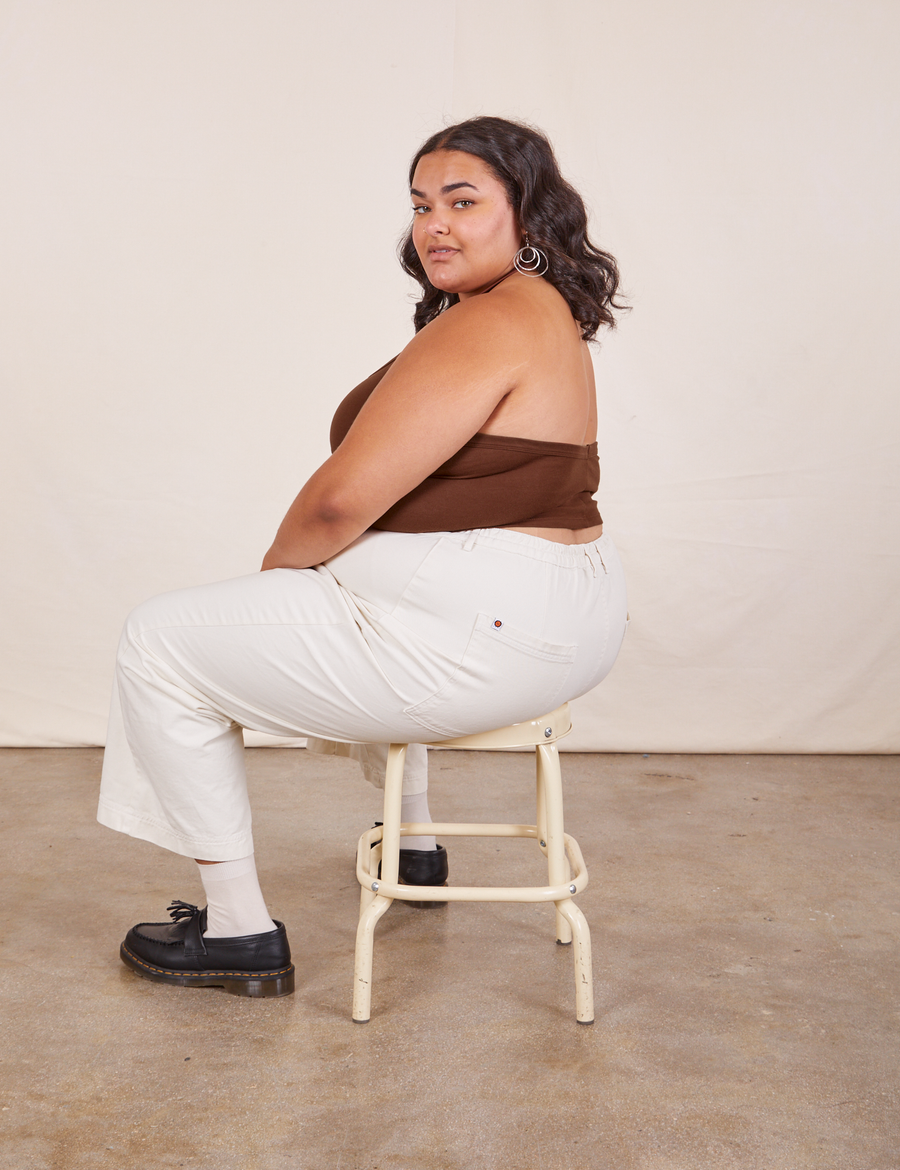 Alicia is sitting on a vintage stool facing the left side. She is wearing Halter Top in Fudgesicle Brown and vintage off-white Western Pants.