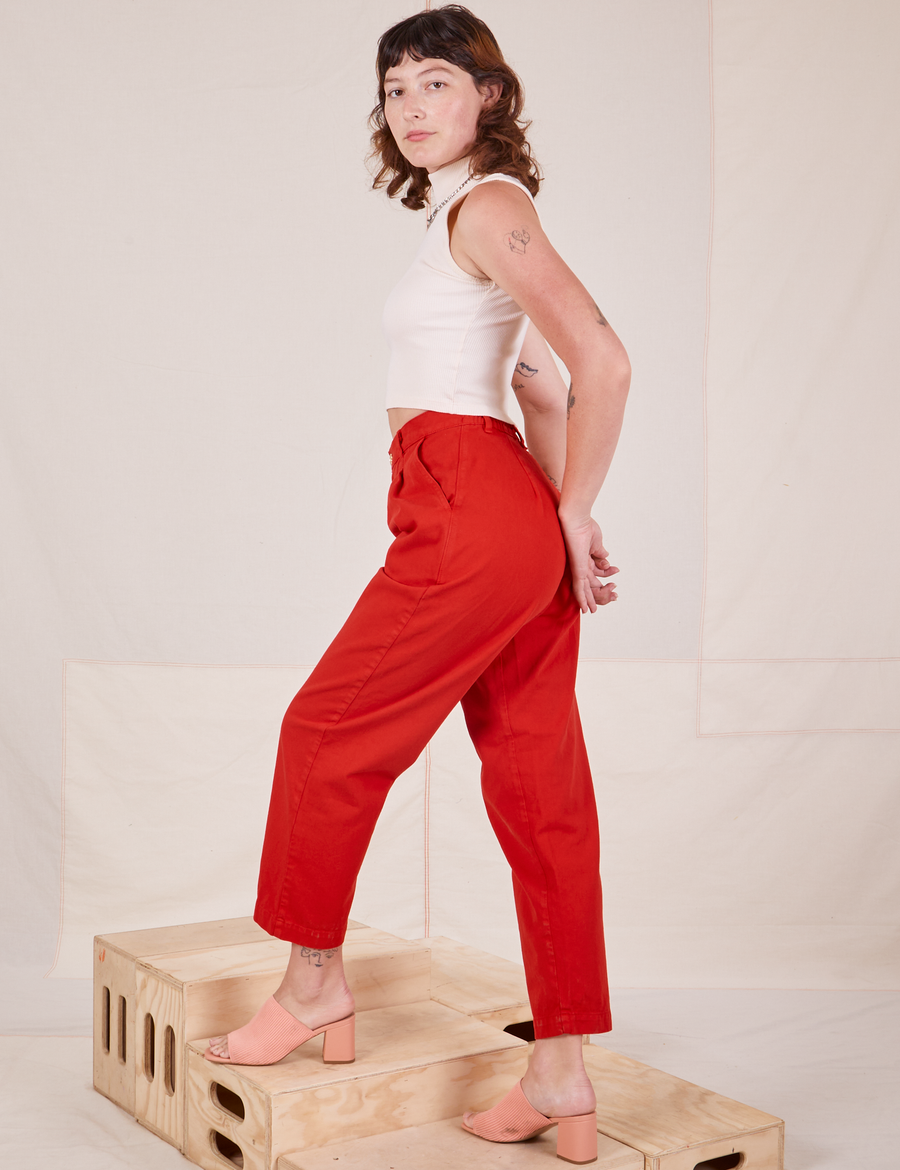 Angled side view of Heavyweight Trousers in Mustang Red and vintage off-white Sleeveless Turtleneck worn by Alex