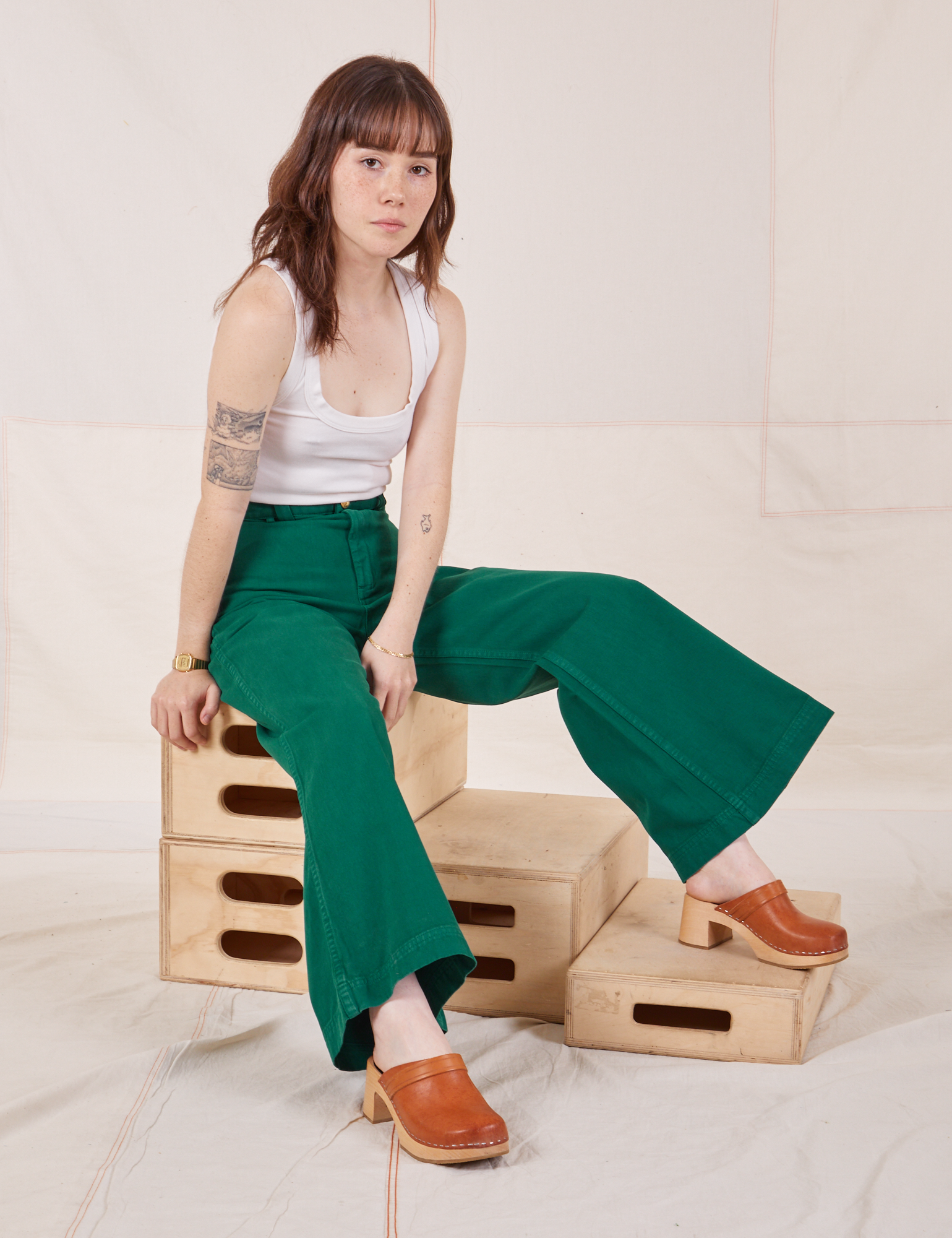 Hana is sitting on a stack of wooden crates wearing Bell Bottoms in Hunter Green