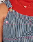 Front close up of Railroad Stripe Denim Original Overalls worn by Morgan. Red contrast stitching and red and white sun baby logo tag