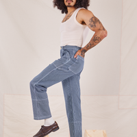 Side view of Carpenter Jeans in Railroad Stripes and vintage off-white Tank Top worn by Jesse