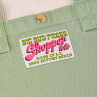 Sun Baby brass snap on Shopper Tote Bag in Sage Green. Bag label with green and pink text that reads "Big Bud Press Shopper Tote, Made in L.A., 100% Cotton Denim" on white background