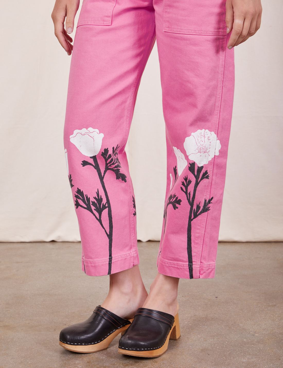 Pant leg close up of California Poppy Overalls in Bubblegum Pink. Paintstamped white poppies with black stems and leaves