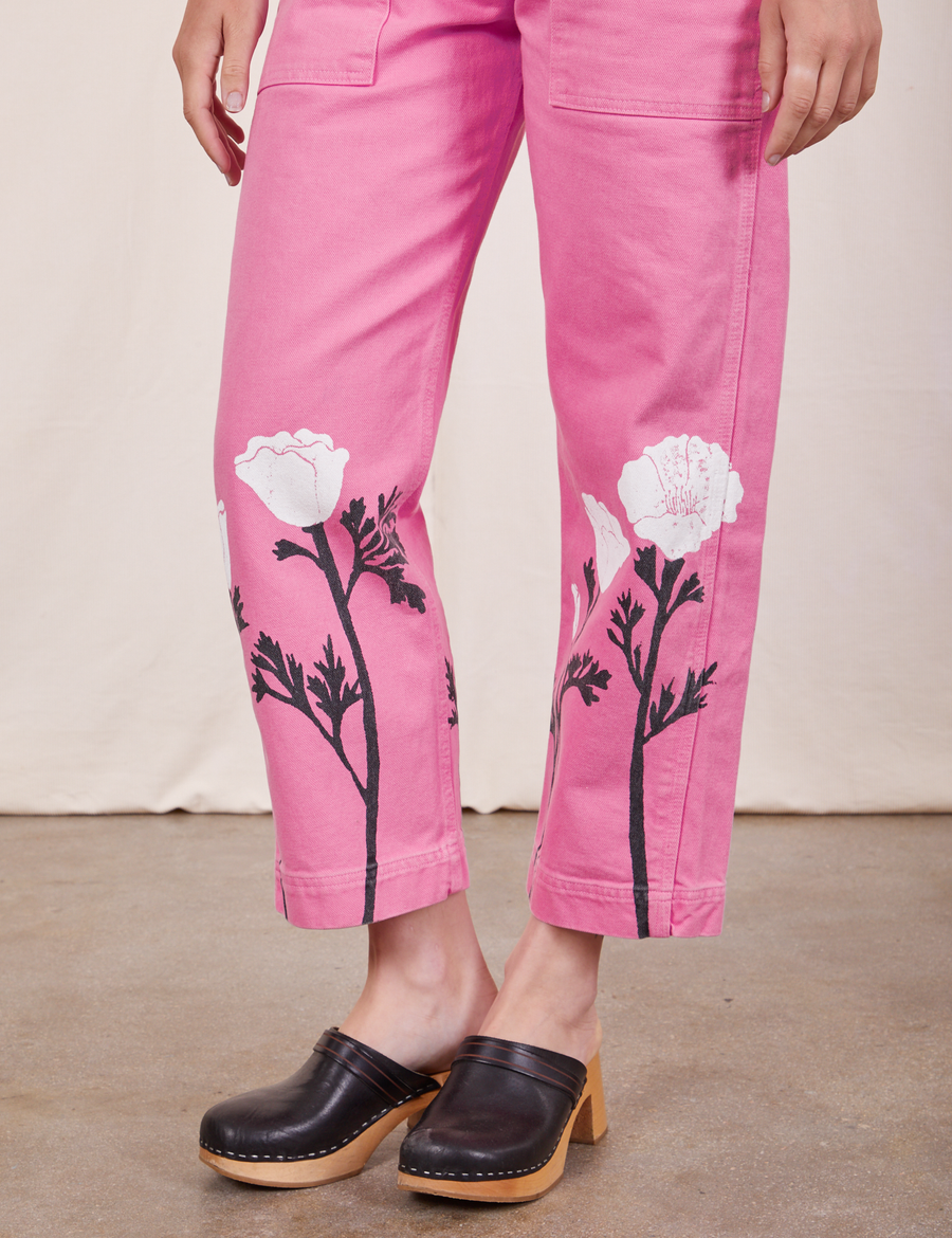 Pant leg close up of California Poppy Overalls in Bubblegum Pink. Paintstamped white poppies with black stems and leaves