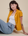Alex is sitting on the ground wearing Pantry Button-Up in Mustard Yellow