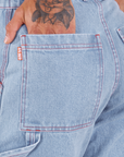 Back pocket close up of Carpenter Jeans in Light Wash. Jesse has their hand in the pocket.