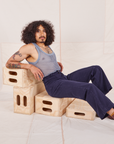 Jesse is sitting on a wooden crate wearing Mesh Tank Top in Periwinkle and navy Western Pants
