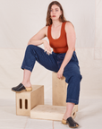 Allison is sitting on a wooden crate wearing Denim Trouser Jeans in Dark Wash and a burnt orange Tank Top