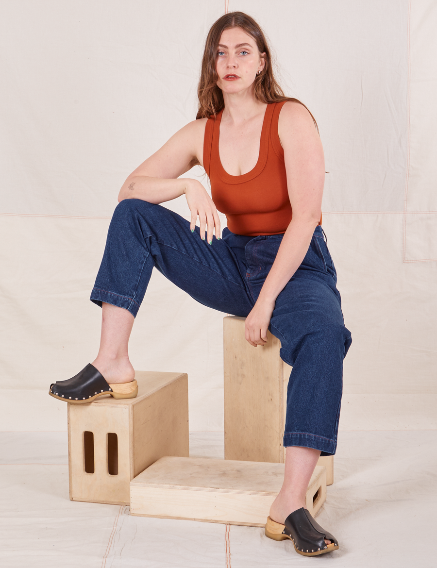 Allison is sitting on a wooden crate wearing Denim Trouser Jeans in Dark Wash and a burnt orange Tank Top