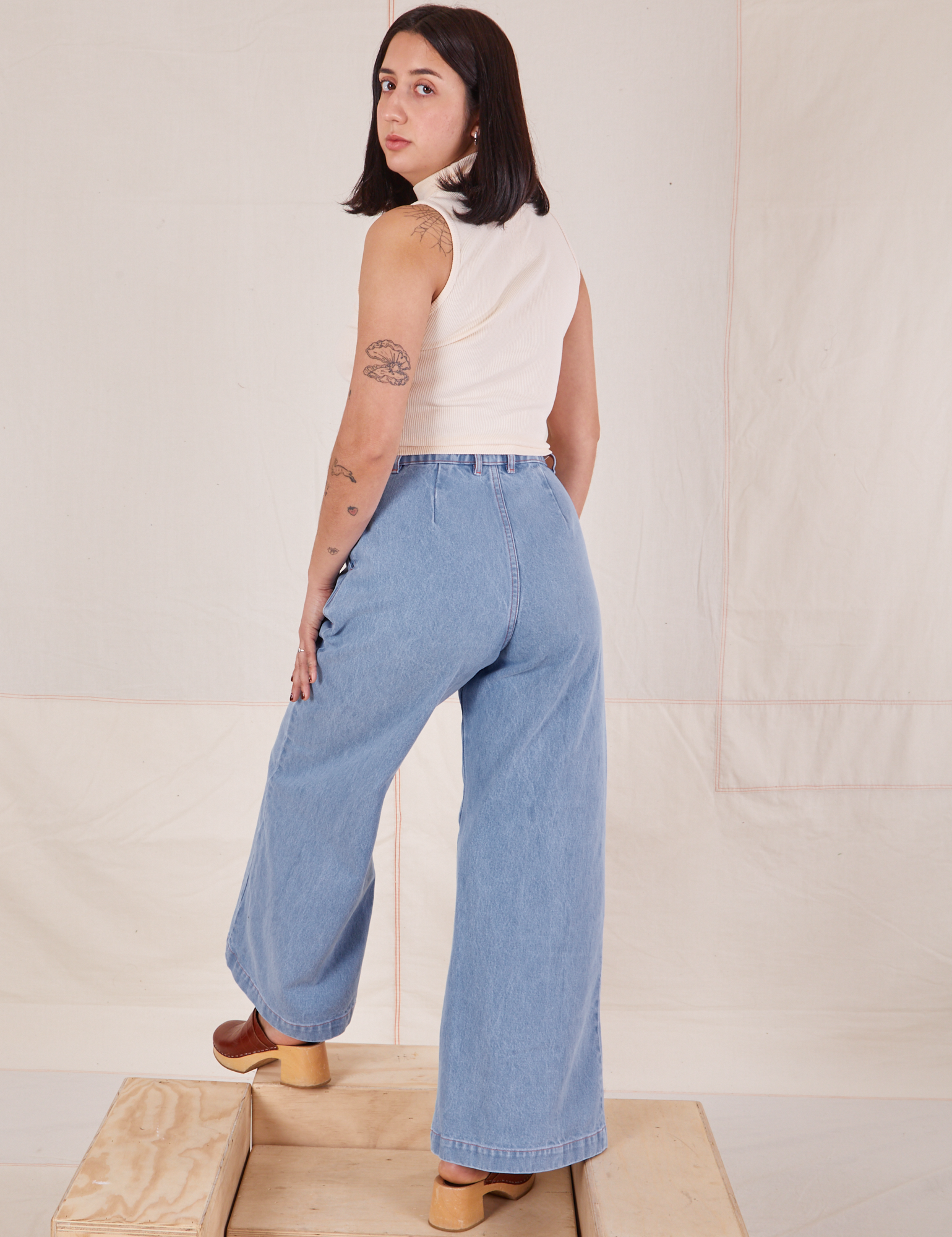 Back view of Indigo Wide Leg Trousers in Light Wash and vintage off-white Sleeveless Turtleneck on Betty