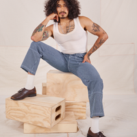 Jesse is sitting on a stack of wooden crates. They are wearing Carpenter Jeans in Railroad Stripes and vintage off-white Tank Top.