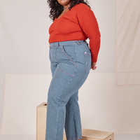 Side view of Railroad Stripe Denim Work Pants and paprika Long Sleeve V-Neck Tee worn by Morgan
