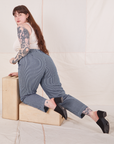Sydney is kneeling on a wooden crate wearing Denim Trouser Jeans in Railroad Stripe and a vintage off-white Tank Top