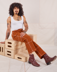 Jesse is sitting on a stack of wooden crates. They are wearing Carpenter Jeans in Burnt Terracotta and vintage off-white Cropped Tank Top