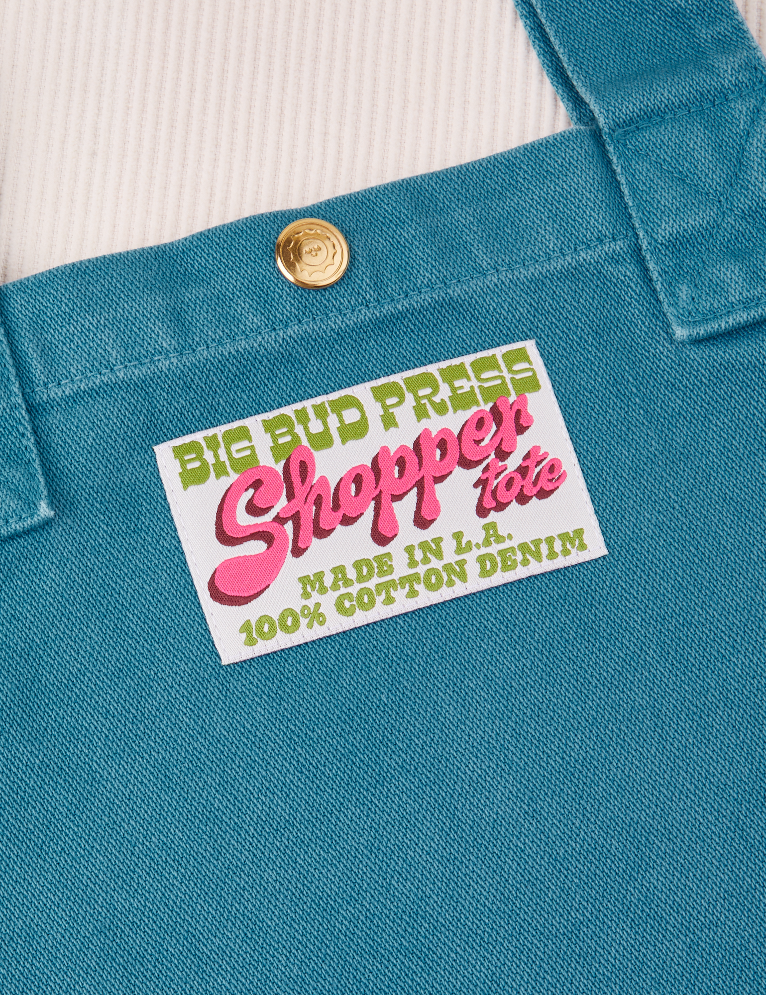 Sun Baby brass snap on Shopper Tote Bag in Marine Blue. Bag label with green and pink text that reads &quot;Big Bud Press Shopper Tote, Made in L.A., 100% Cotton Denim&quot; on white background