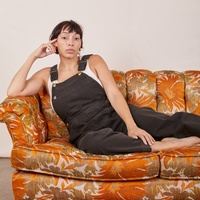 Tiara is wearing Original Overalls in Mono Espresso and sitting on a floral couch.