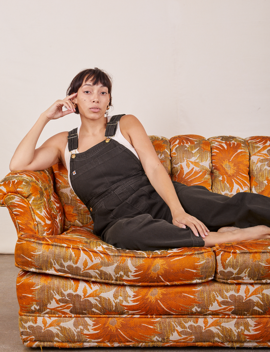 Tiara is wearing Original Overalls in Mono Espresso and sitting on a floral couch.