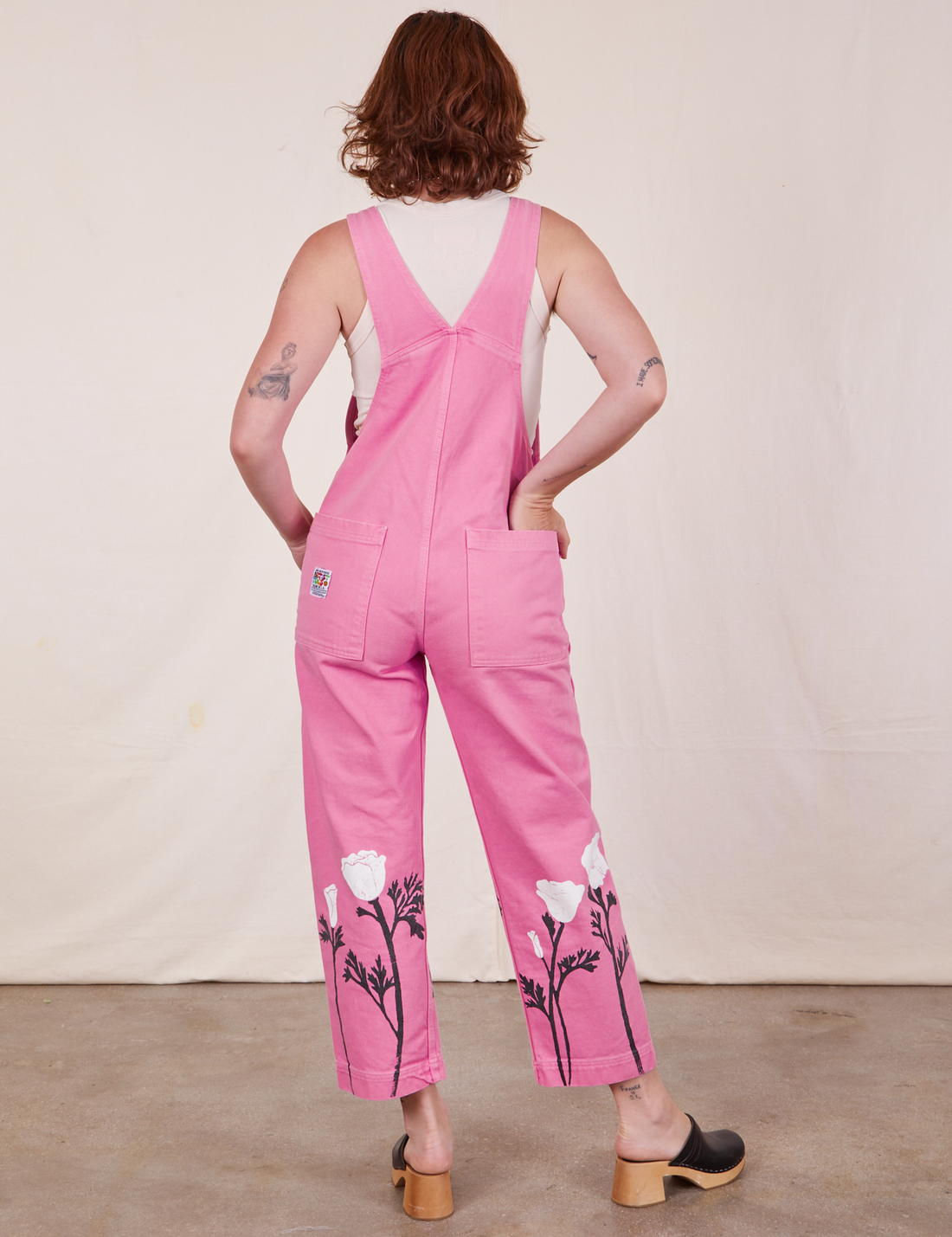Back view of California Poppy Overalls in Bubblegum Pink and vintage off-white Tank Top underneath. Alex has one hand tucked into the back pocket.
