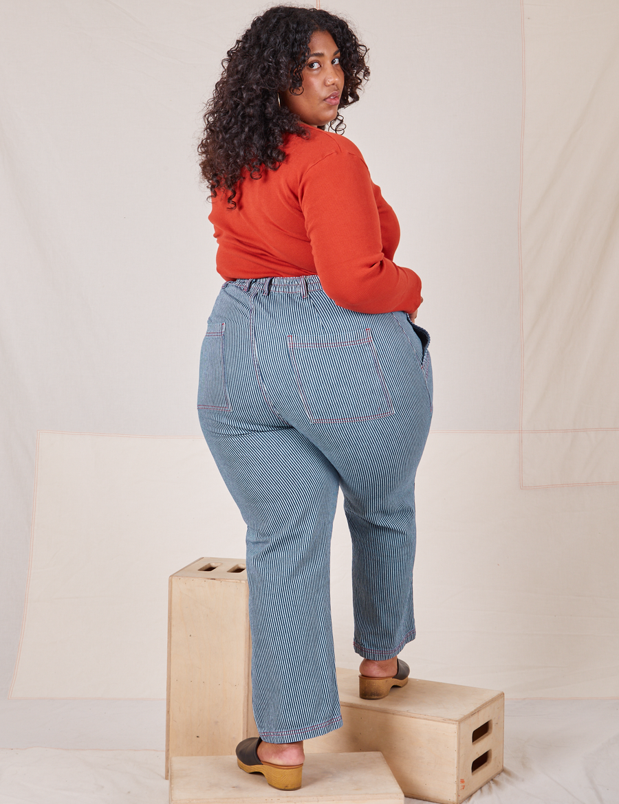 Back view of Railroad Stripe Denim Work Pants and paprika Long Sleeve V-Neck Tee worn by Morgan