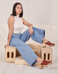Betty is sitting on a wooden crate and wearing Indigo Wide Leg Trousers in Light Wash