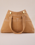 Overall Handbag in Tan with handle strap hanging down front of bag.