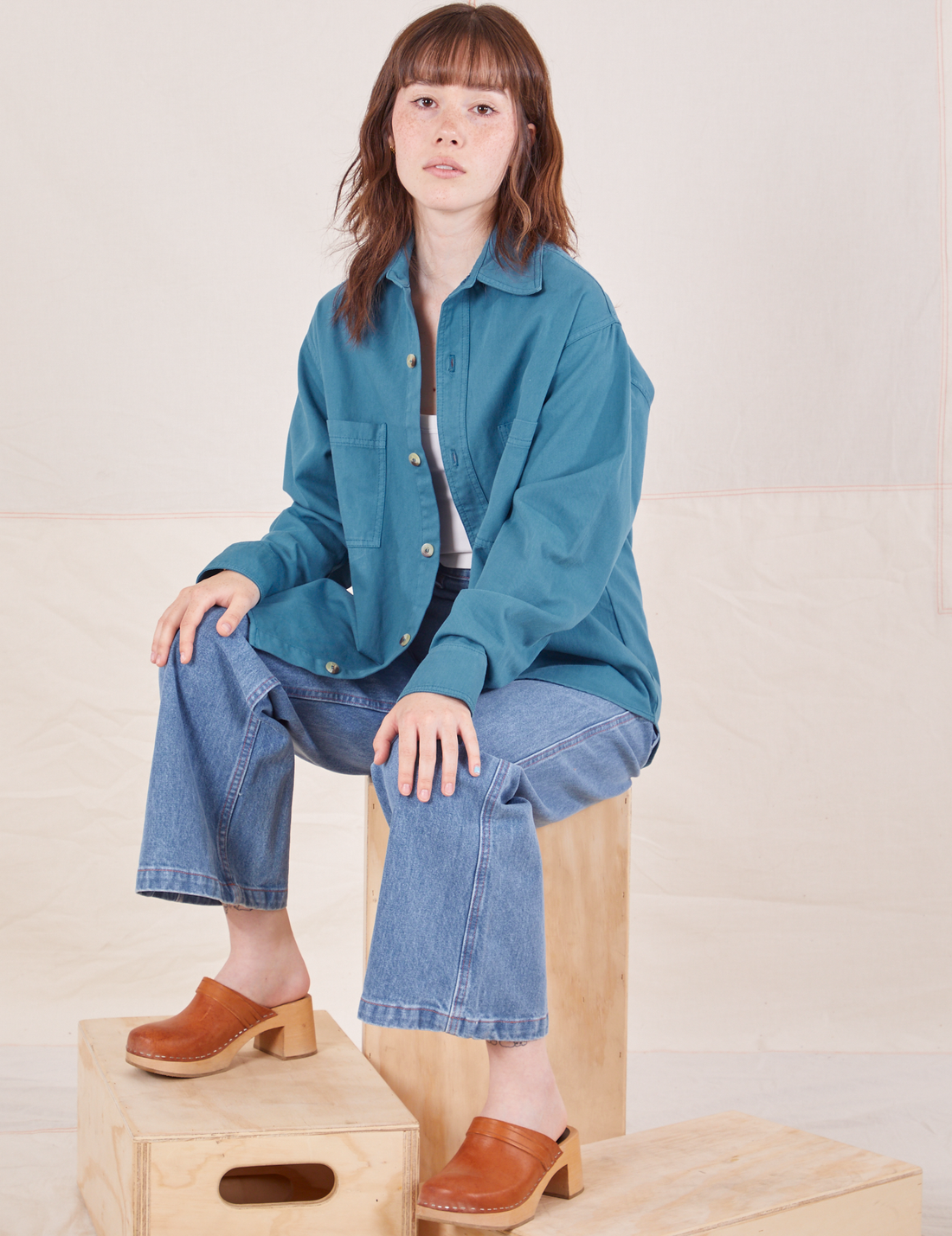 Hana is sitting on a wooden crate wearing Oversize Overshirt in Marine Blue