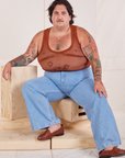 Sam is sitting on a wooden crate wearing Mesh Tank Top in Burnt Terracotta and light wash Sailor Jeans