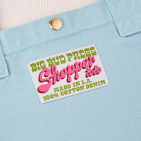 Sun Baby brass snap on Shopper Tote Bag in Baby Blue. Bag label with green and pink text that reads "Big Bud Press Shopper Tote, Made in L.A., 100% Cotton Denim" on white background